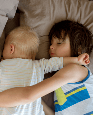 Toddler with his arm around his sleeping baby brother