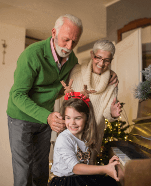 Child playing piano while her Grandparents stand behind her and enjoy the music