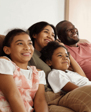 Family of 4 snuggled on the couch, smiling, and watching a movie together