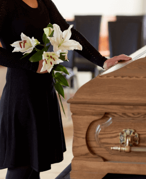 Women holding flowers at a funeral while touching a casket