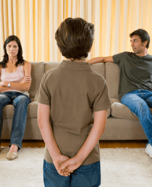 child standing in front of his parents while they talk on the couch