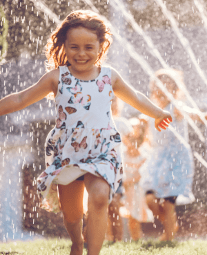 Young child running through a sprinkler and playing independently