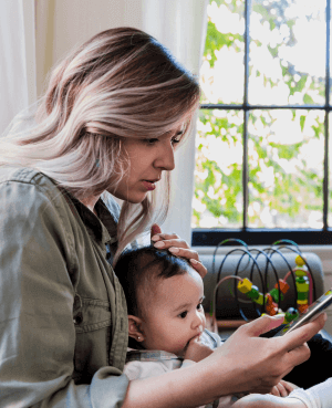 A mother on her phone while holding her baby