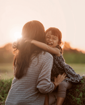 A child with a wide smile happily embraces an adult, representing a strong, secure attachment and healthy parent-child relationship.