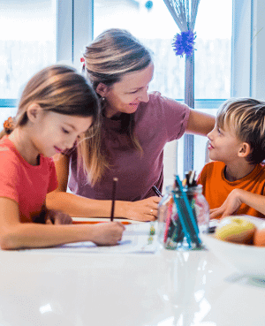 Parent gently assisting two children with homework or drawing, illustrating scaffolding in parenting for skill-building.
