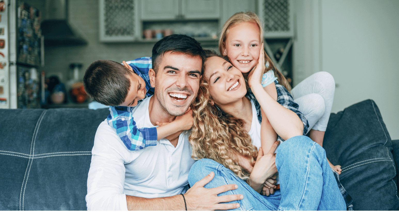 Happy family on a couch, with parents smiling and two children embracing them, symbolizing a strong and connected family.