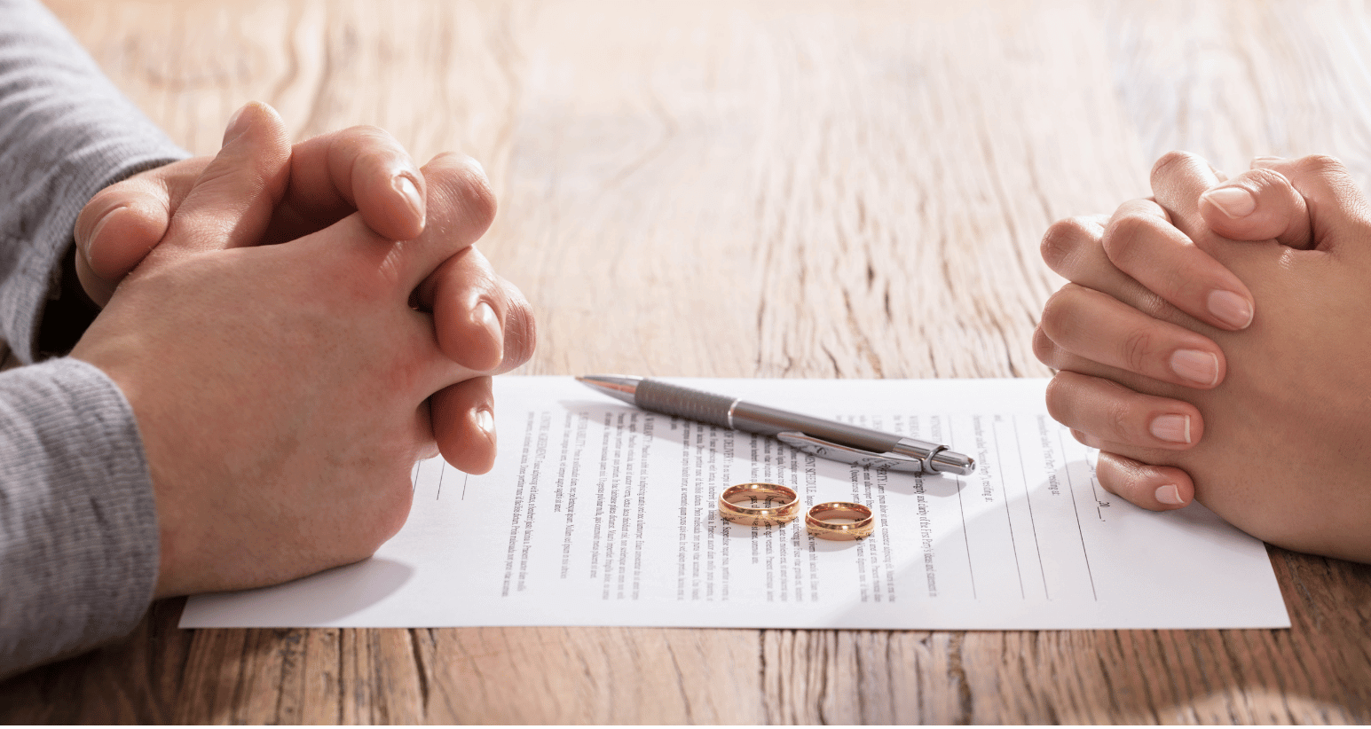 A couple's hands rest on a divorce agreement with wedding rings and a pen.