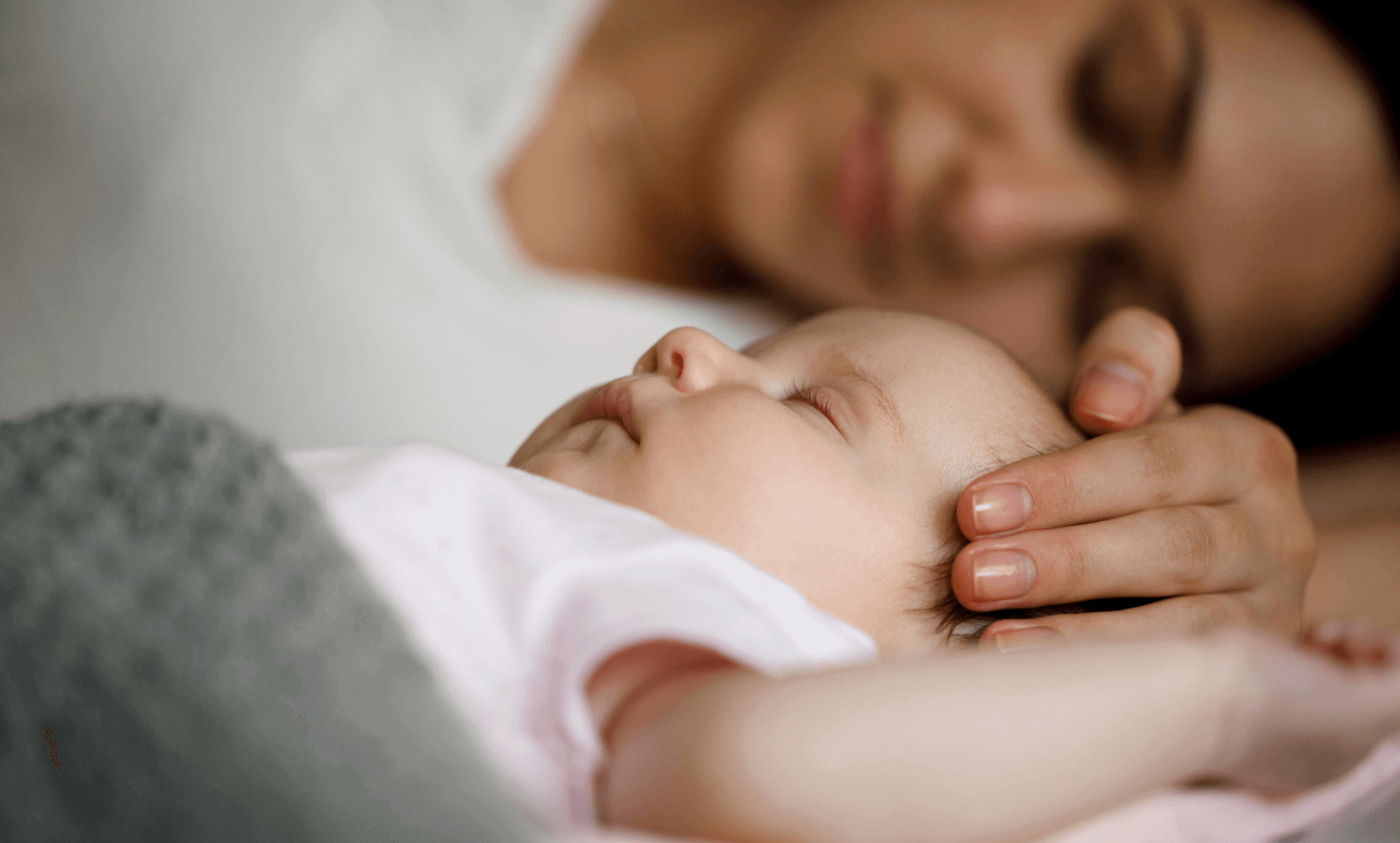 Close-up of a newborn baby peacefully sleeping while a parent's hand gently rests on their head, symbolizing the comfort of contact sleep and nurturing for healthy baby sleep development.