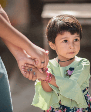 Young child holding adult’s hand, looking uncertain, symbolizing anxiety or resistance.