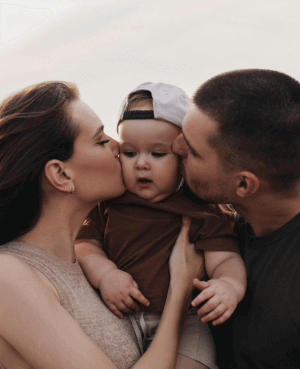 Happy parents, a man and a woman, kissing their baby on the cheeks, showing love and family connection after kids.