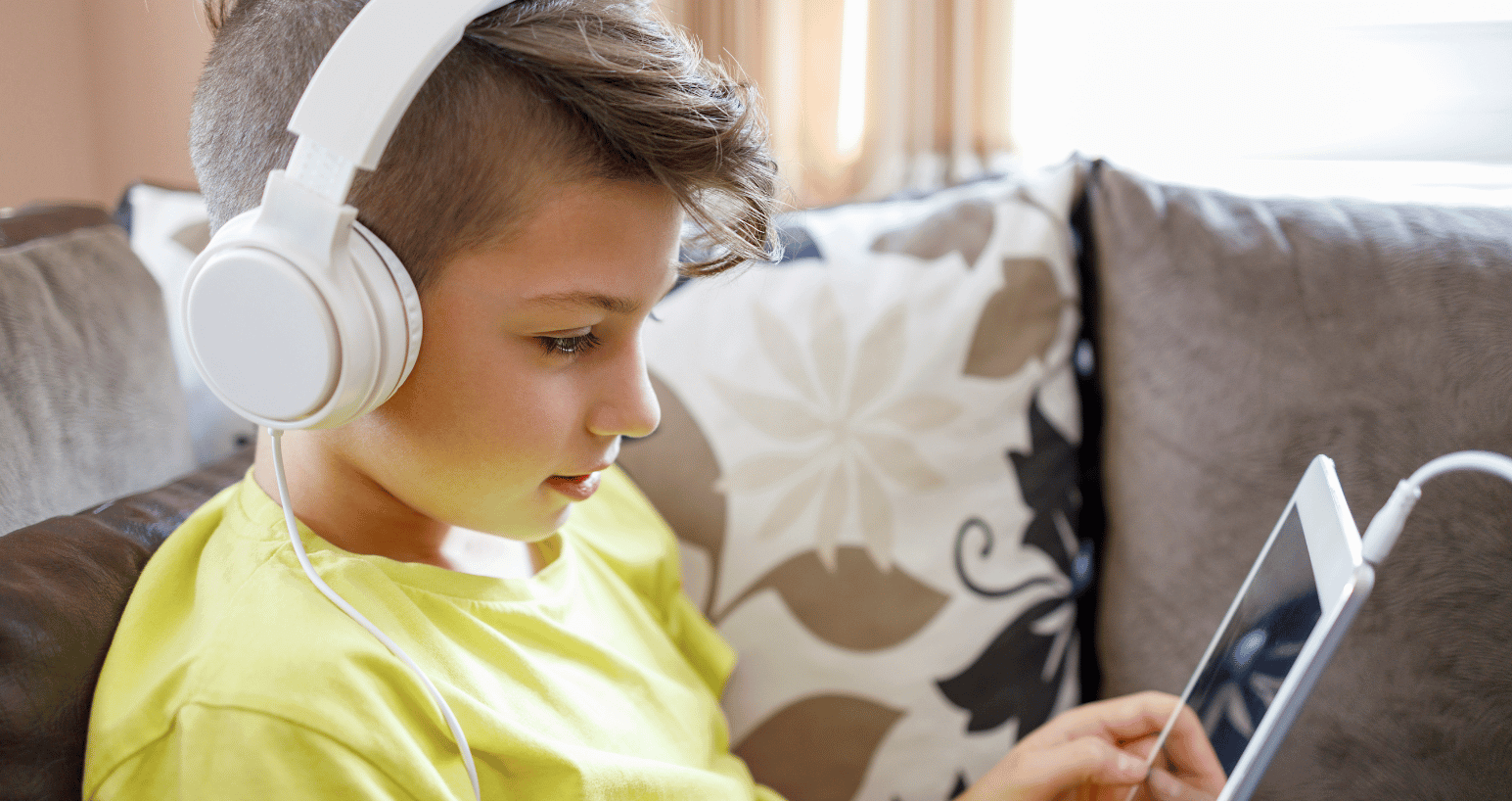 Boy wearing white headphones watching a tablet.