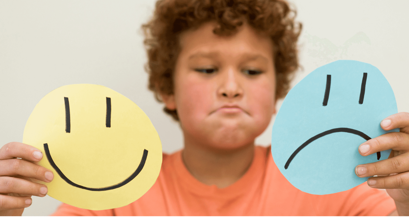 Child holding paper cutouts of happy and sad faces, reflecting emotional awareness.