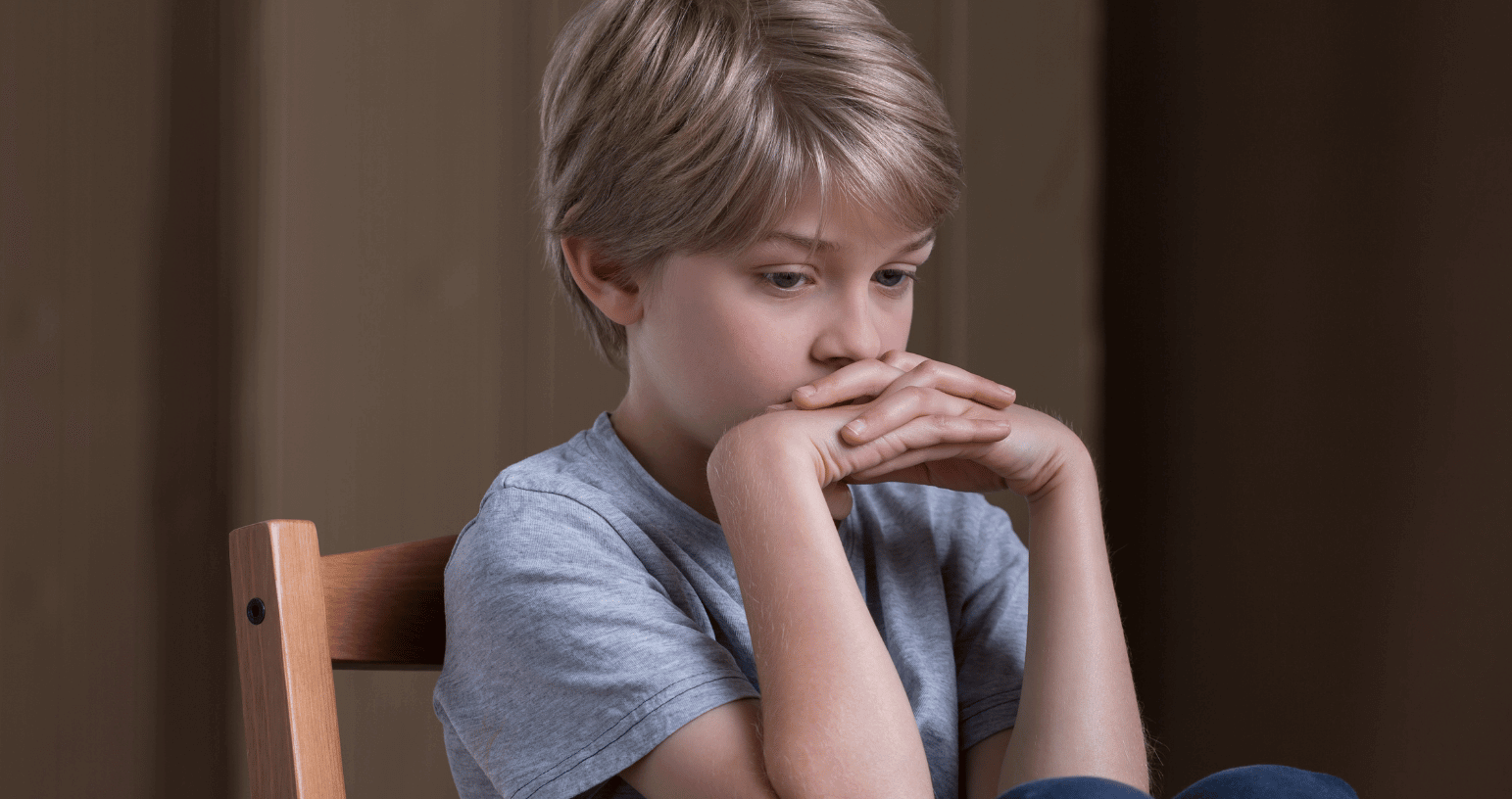 Thoughtful young boy sitting with his hands near his mouth, appearing deep in thought or concerned.
