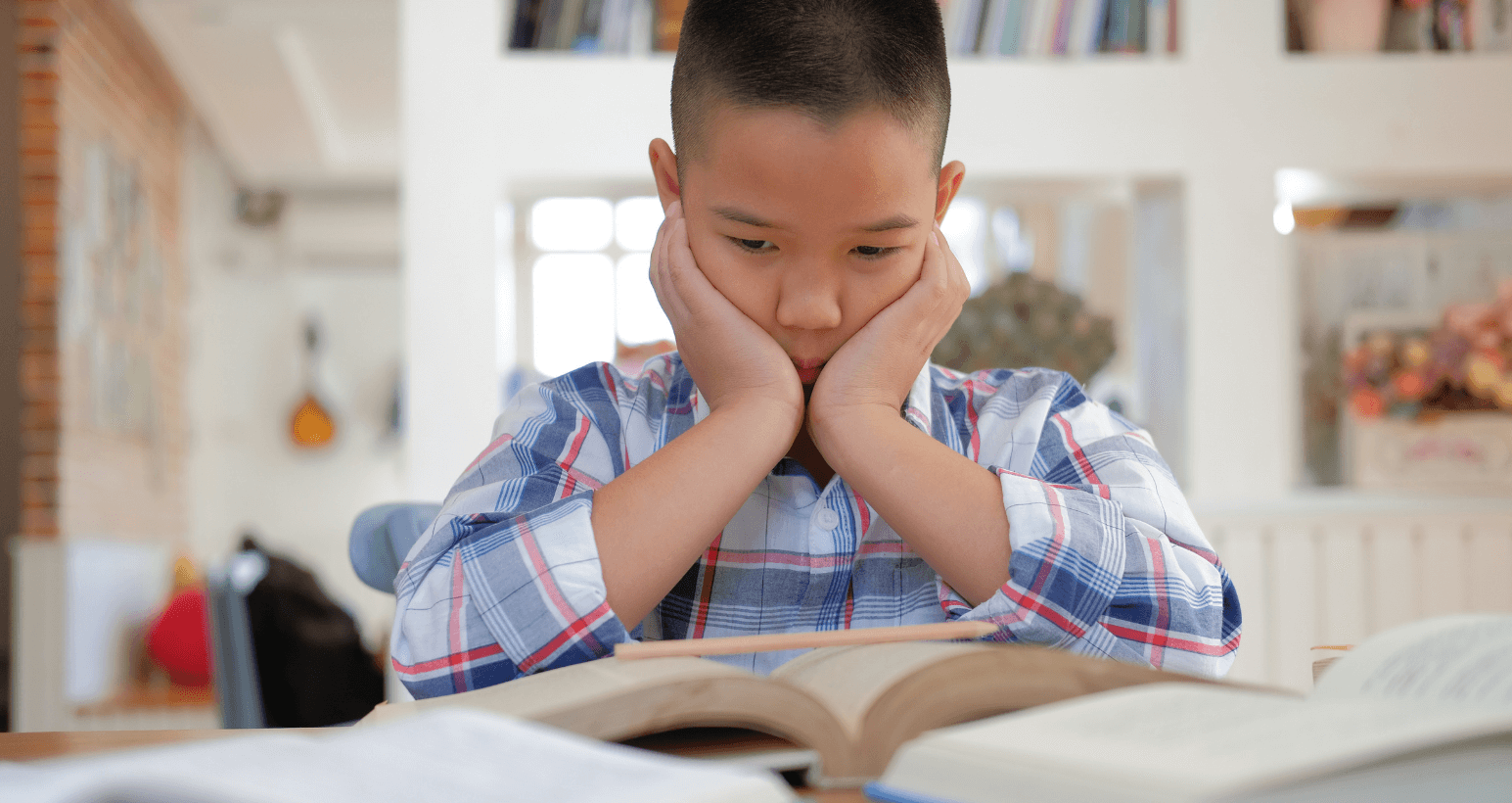 Sad elementary school boy sitting at a desk with open books, looking discouraged and overwhelmed.