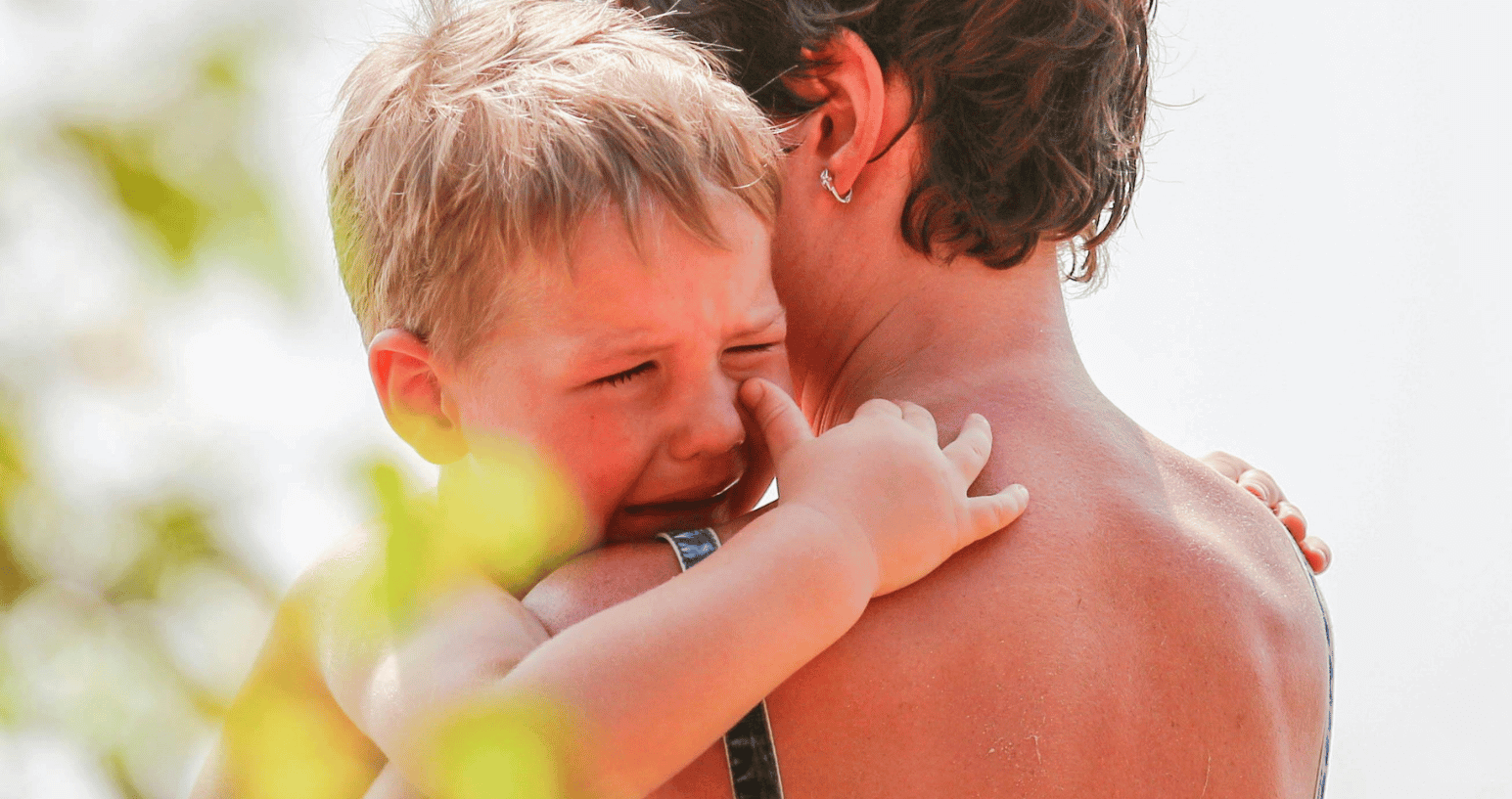 Upset young boy crying while being comforted by a parent outdoors.