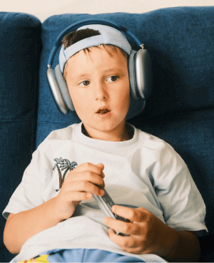 Boy listening to music with over-ear headphones while holding a smartphone.