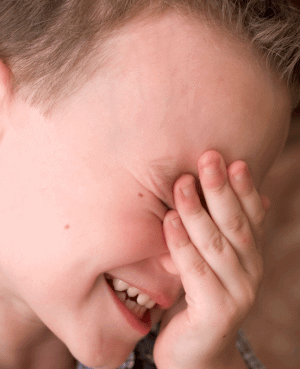 Young boy covering his face with his hand, expressing shyness or embarrassment.