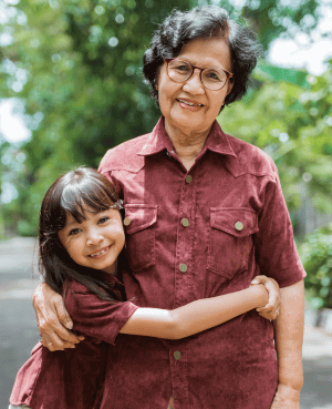 Smiling grandmother embraces her young granddaughter outdoors.