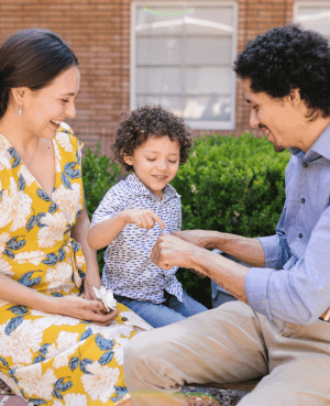 Parents sit outside with their young son, smiling and connecting.