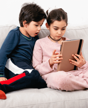 Two children sitting on a couch using a tablet together.
