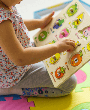 Toddler plays independently with a puzzle book on a foam mat.