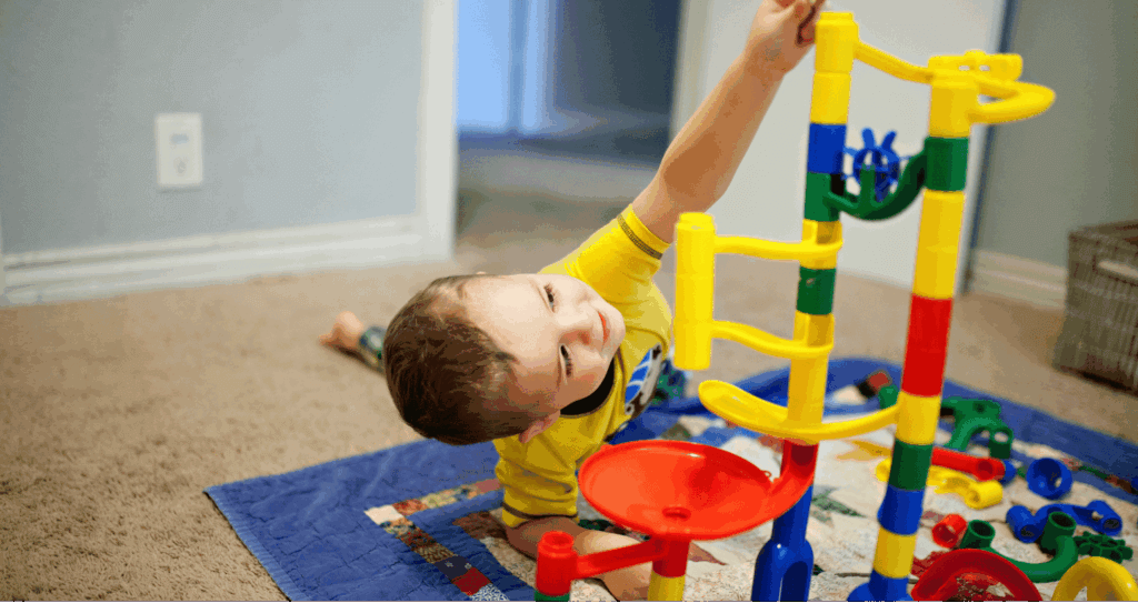 Young boy builds a marble run independently on the floor.