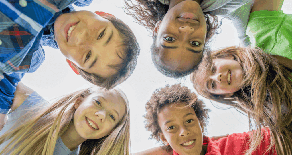 Diverse group of children smiling in a circle outdoors.