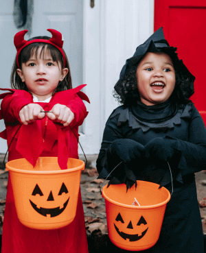Two young children dressed as Halloween characters holding pumpkin buckets.