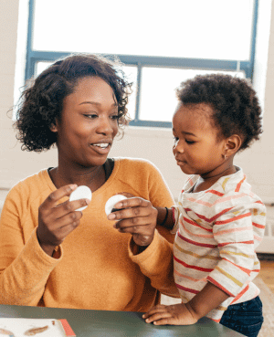 Mother showing a young child two circular objects during a playful learning activity.