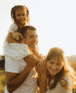 Parents smiling with child on shoulders at sunset, showing joyful connection.