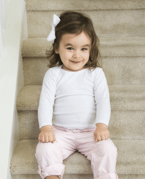 Smiling toddler girl sitting on stairs in a white shirt.