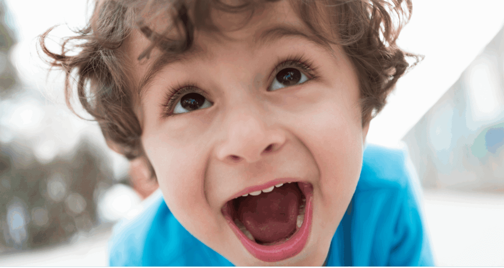 Close-up of a young child smiling with wide open mouth and expressive face.