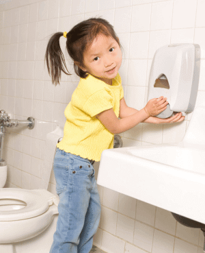 Young child washing hands at a sink after using the bathroom.