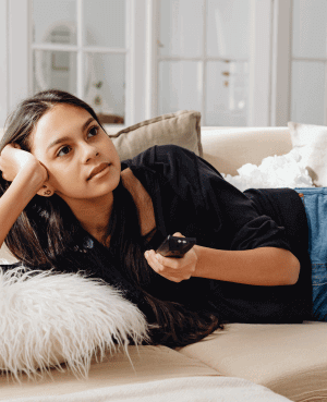 Young person watching TV with a pensive expression, symbolizing media overwhelm.