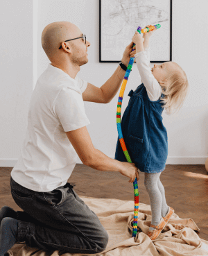 Parent supporting a young child building a tall tower with colorful blocks.