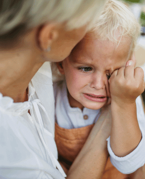 Caregiver holding a crying toddler close and gently reassuring them.