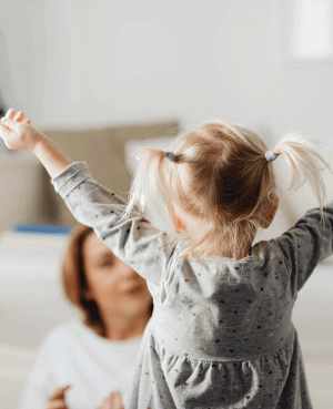Toddler with arms raised toward a caregiver, showing energy, confidence, and a desire for connection.