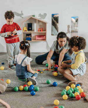 Therapist sitting on the floor playing with young children using colorful balls during a group activity.
