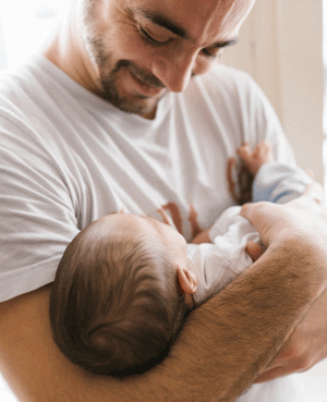 Father smiling while cradling a newborn baby in his arms.