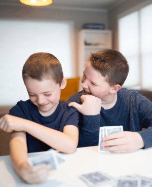 Two boys playing cards, one teasing the other while he looks upset.