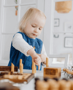 Toddler playing with wooden blocks at a table, illustrating independent play skills.
