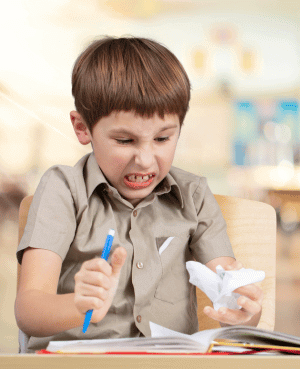 Child crumpling paper in frustration during homework, a common perfectionism moment.