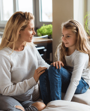 Parent talking calmly with a child on a couch, modeling co-regulation and support.