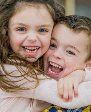 Two young children hugging and smiling, showing warmth and sibling connection.