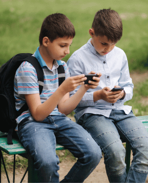 Two preteen boys sitting outdoors on a bench, both absorbed in their smartphones, illustrating screen time and social media use in children.