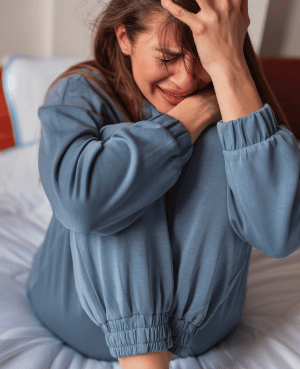 Distressed parent sitting on bed with hands on head, reflecting the overwhelm of navigating a child's sudden behavioral changes.