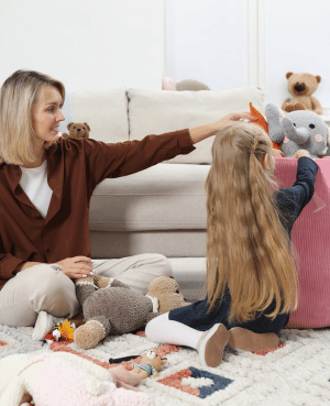 Parent and toddler cleaning up toys together in a living room, showing collaborative cleanup practice.