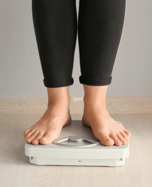 Person standing on a bathroom scale, representing weight related health changes and body image.