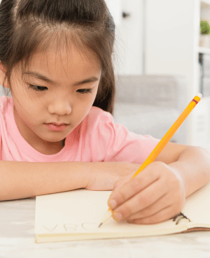 Child writing with a pencil at a desk, representing focused learning and note taking by hand.
