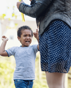 Upset toddler raising his arms toward an adult, showing physical aggression during a dysregulated moment.